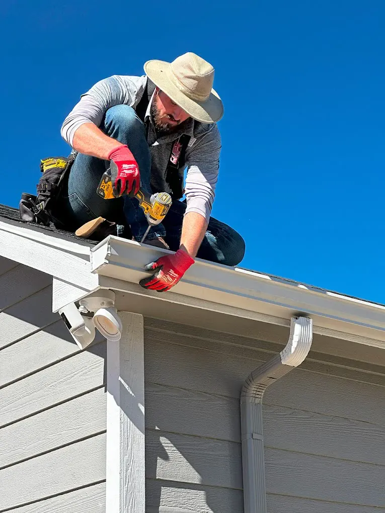 A J.R.B. installer fastening a new white gutter along a roof edge